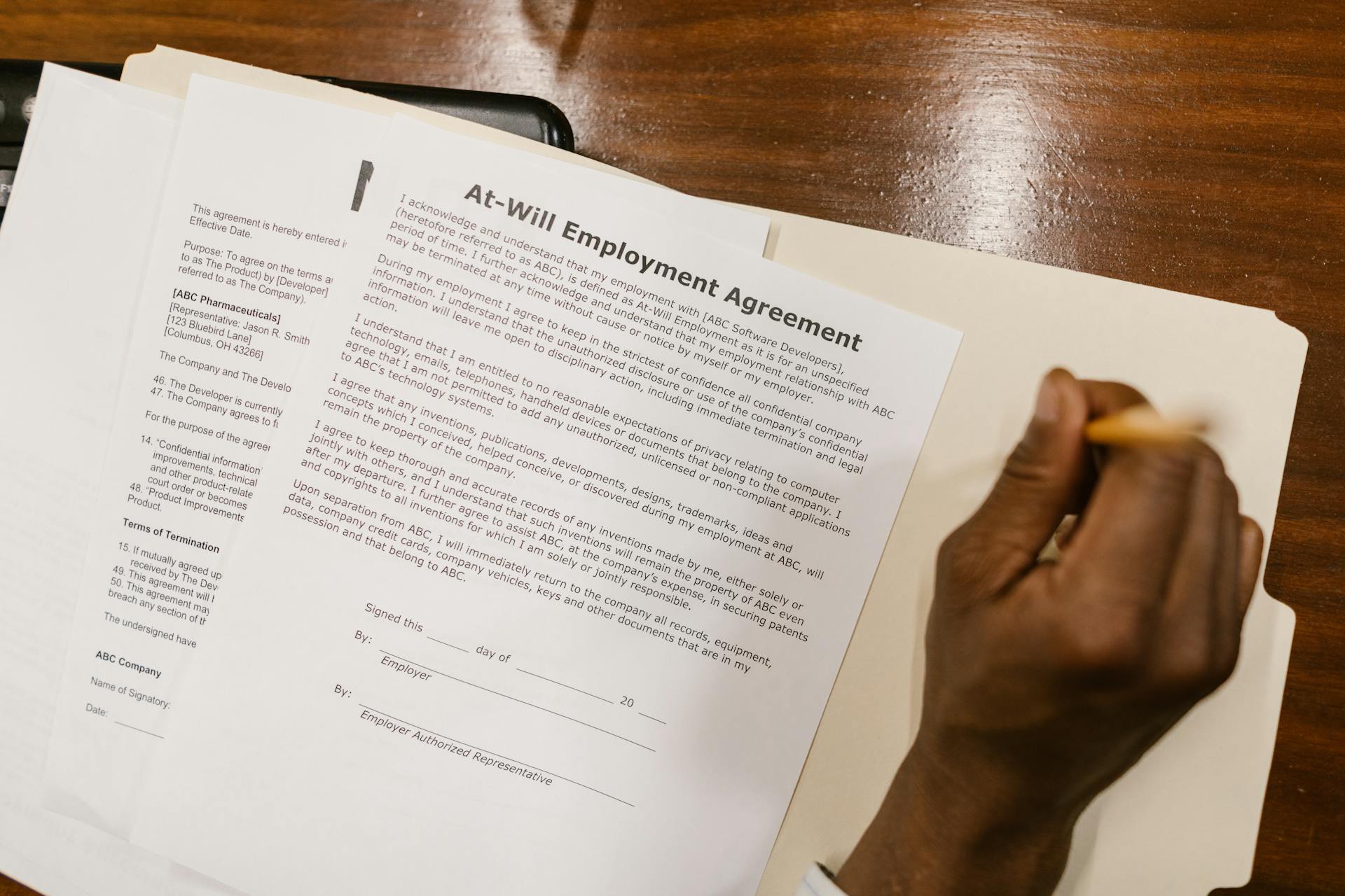 Close-up of a hand signing an at-will employment agreement on a wooden desk.