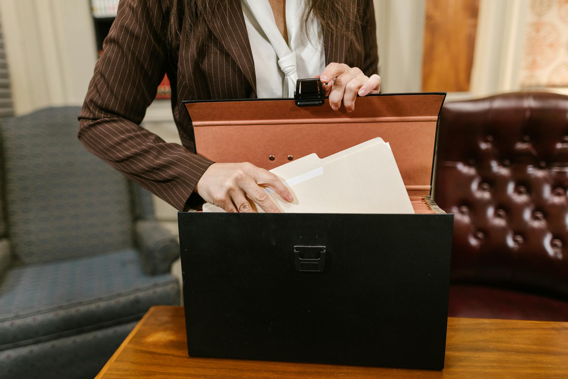 Close-up of a businesswoman organizing files in a black box in an office setting.