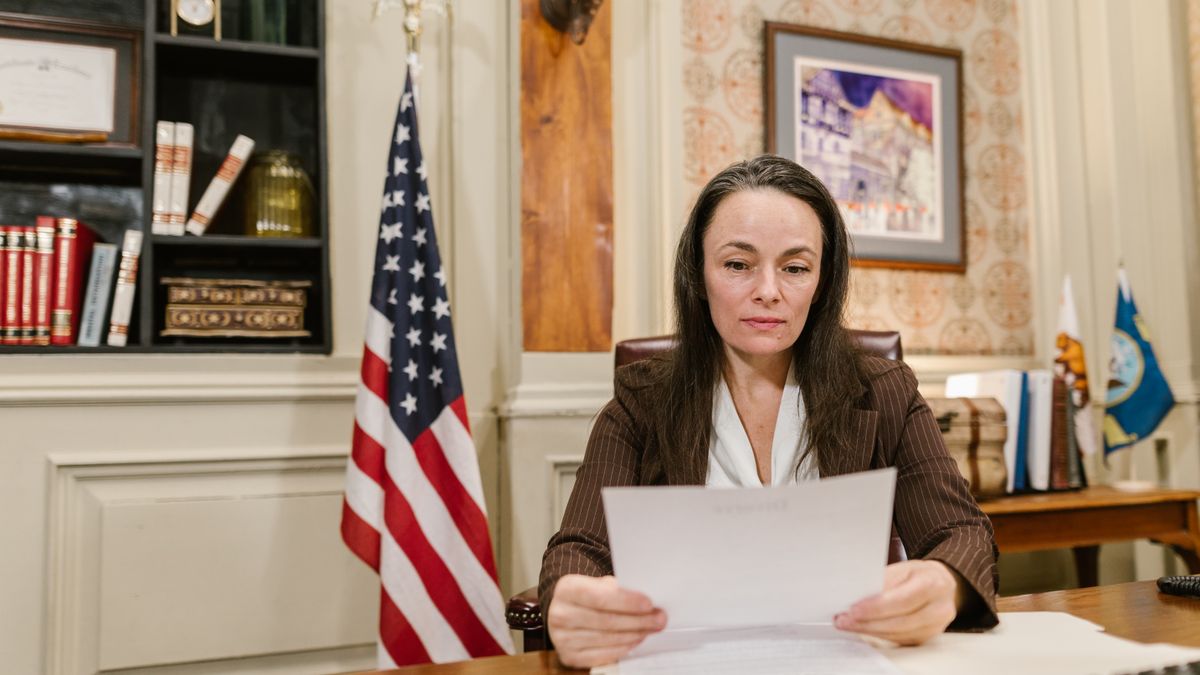 A professional woman reviewing legal documents in an office with flags and books.