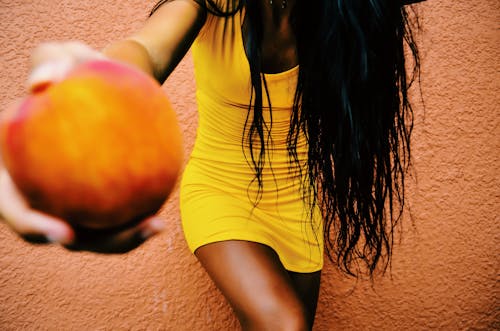 Женщина, держащая круглые фрукты, опираясь на оранжевую стену