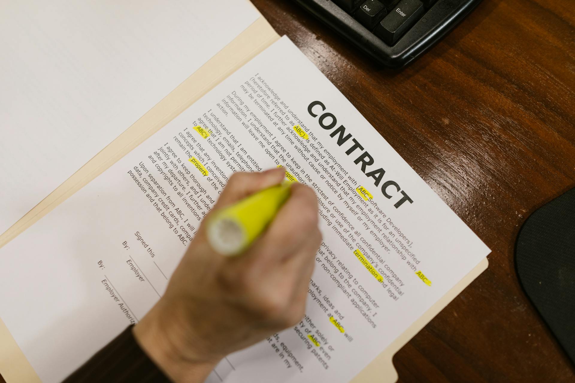 Focused view of a person highlighting text in a contract document on a wooden office desk.