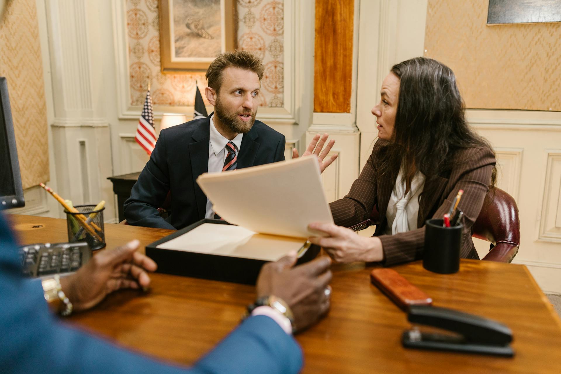 Diverse group in a corporate office engaged in a formal meeting. Professional attire and documents suggest a business discussion.