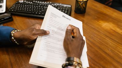 Manos con pulseras firman un documento sobre un escritorio de madera con teclado, sobre posesión efectiva en Chile