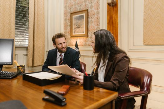 Two professionals engaged in a business discussion in an office setting, reviewing legal documents.