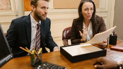 Hombre y mujer en un despacho de madera; ella gesticula sosteniendo un documento, sobre herencia sin testamento Chile