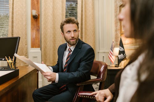 Free A Man in Business Suit Holding a White Paper While Sitting on the Grown Chair Stock Photo