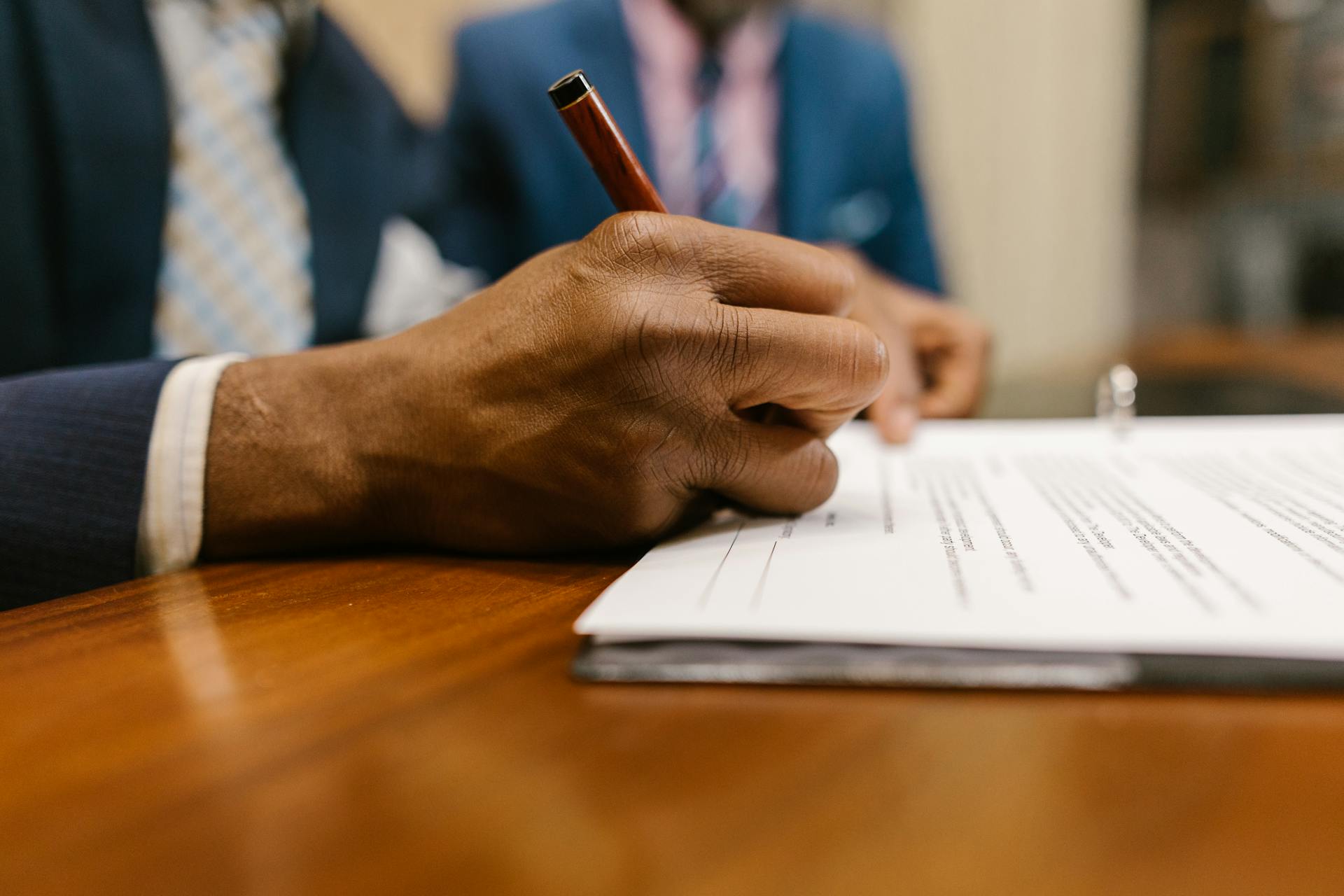 Close-up of an adult signing a legal document with a pen in an office.