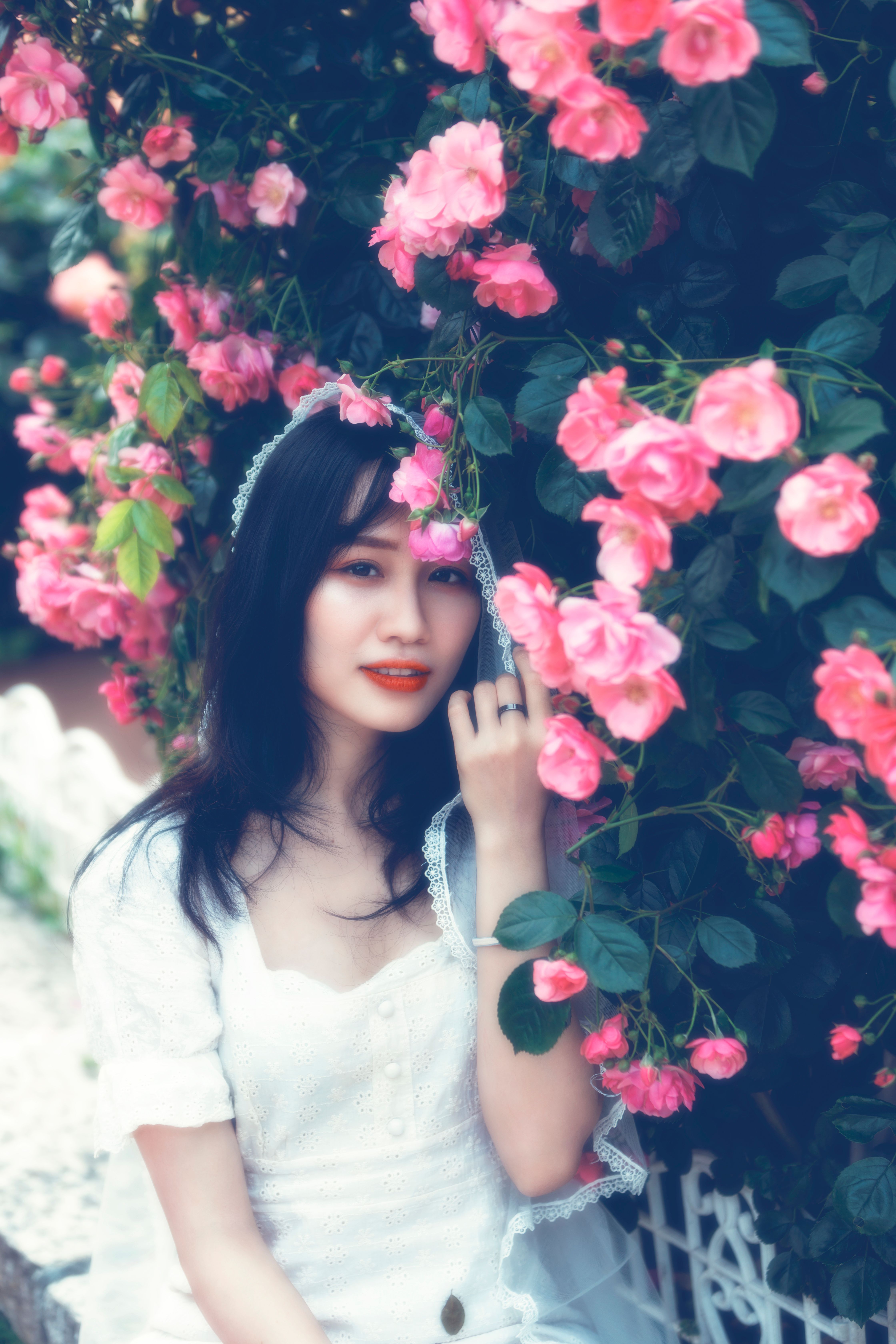 A beautiful woman in a white dress surrounded by vibrant pink flowers outdoors.