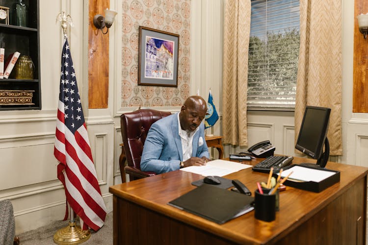 A Man In A Suit Reading A Document On His Work Desk