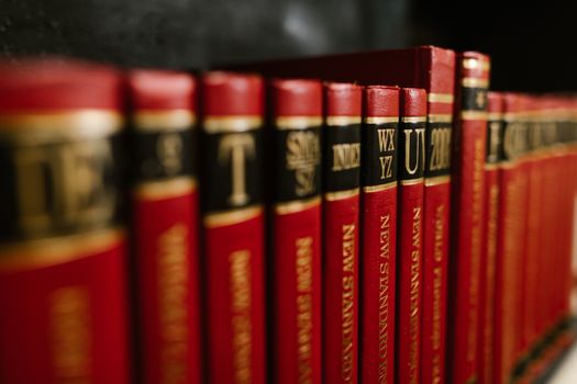 Close-up view of red leather bound encyclopedias on a bookshelf in a library. - Fotografer Sidoarjo