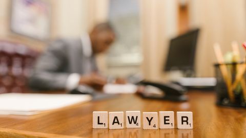 Wooden letter tiles spelling 'LAWYER' on a desk, with blurred office setting in the background.