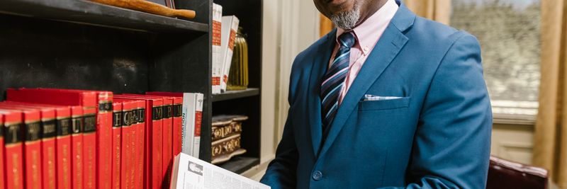 Professional lawyer in formal attire holding a book, smiling in an office setting surrounded by law books.