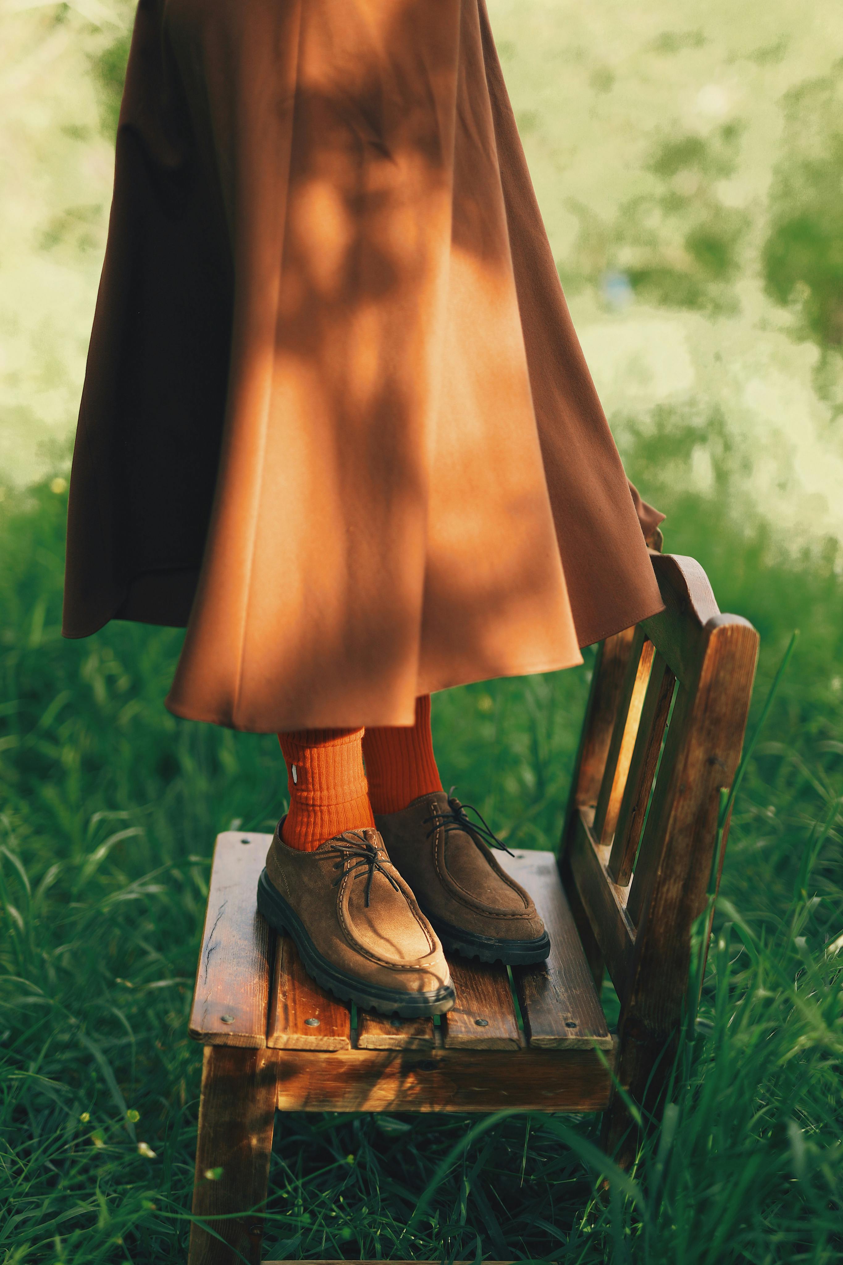 female in stylish skirt standing on wooden chair on green grass