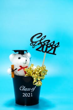 Cute graduation gift with bear, cap, and Class of 2021 decoration on blue background.