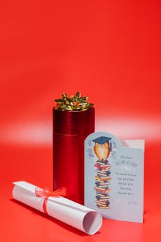Close-up of a graduation gift set with red gift box, diploma, and greeting card on a vivid red background.
