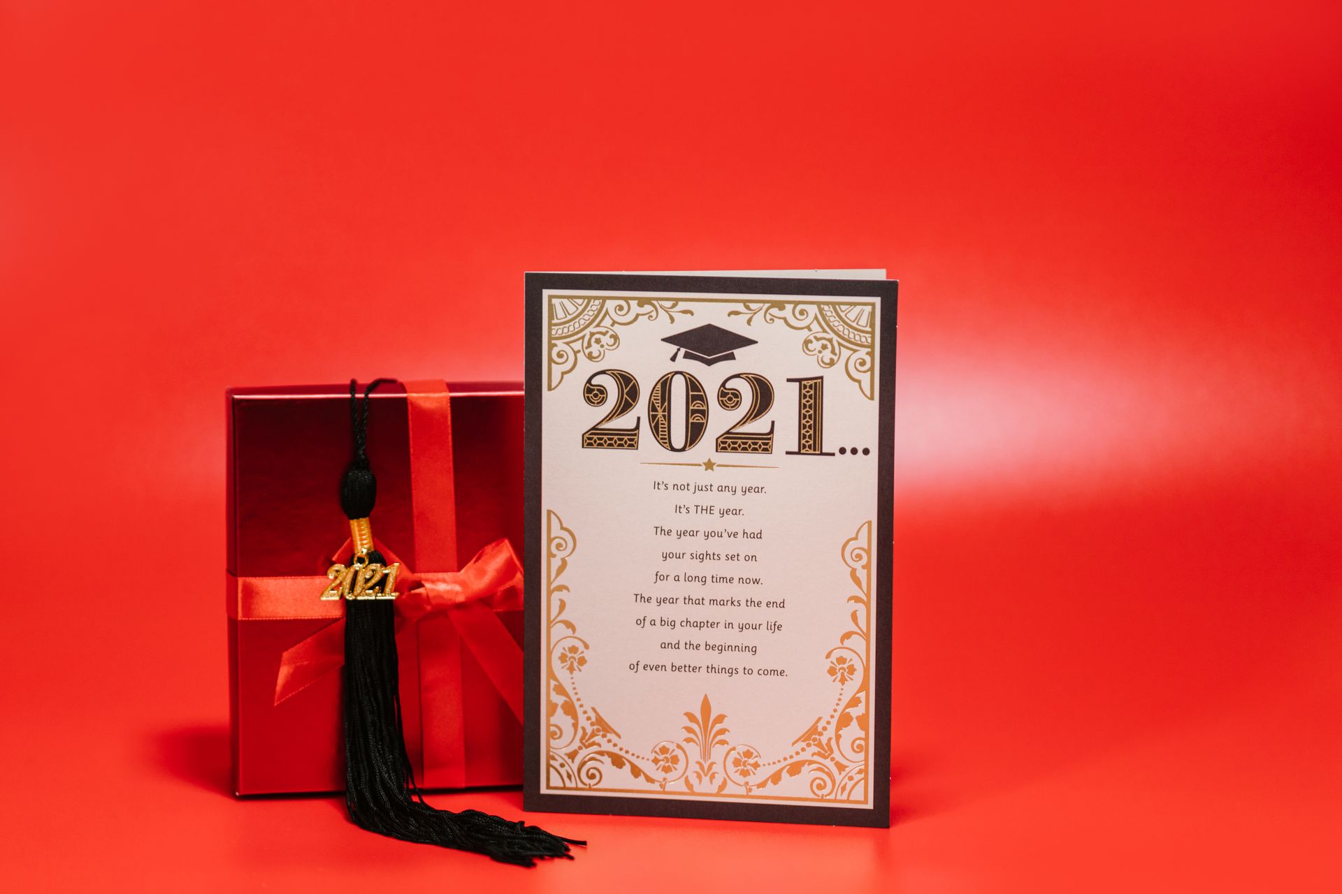 Graduation card and gift box with cap tassel on a bold red background.
