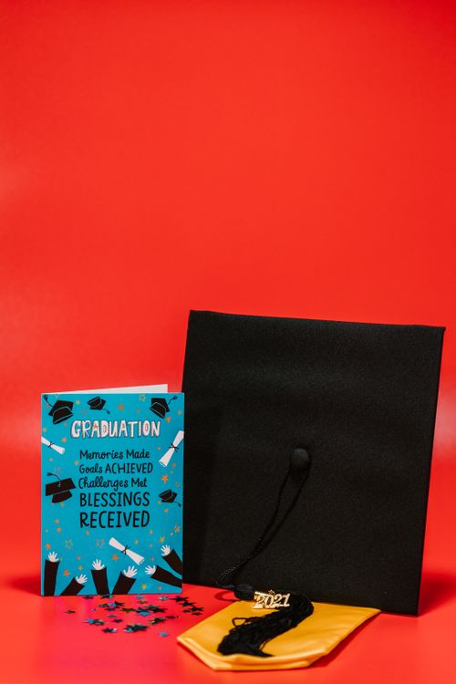 Free Graduation cap and card with a playful design on a bright red background, symbolizing achievement. Stock Photo