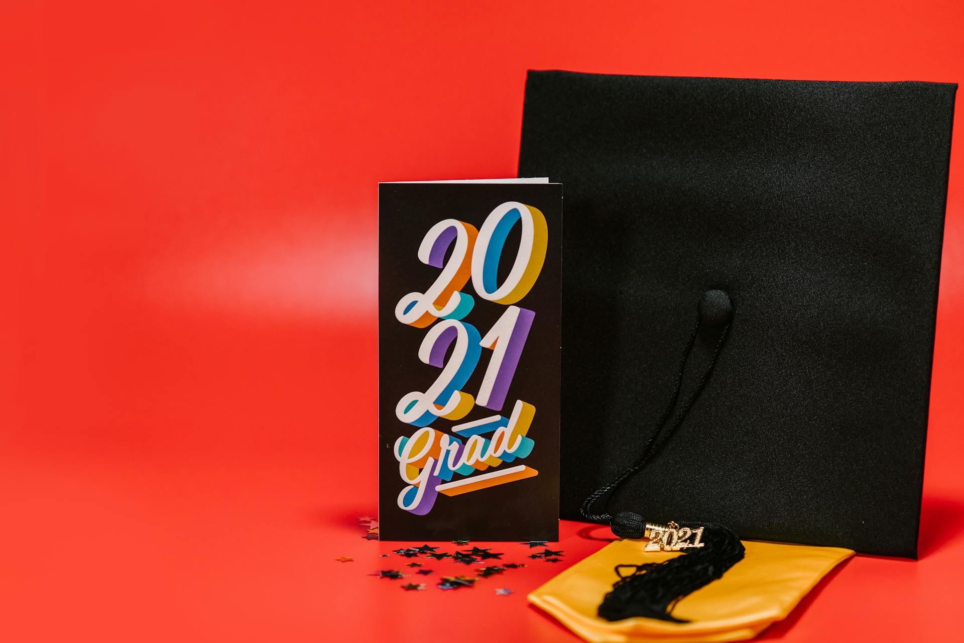 Celebrate graduation with a 2021 cap and multicolored card on a vibrant red background.