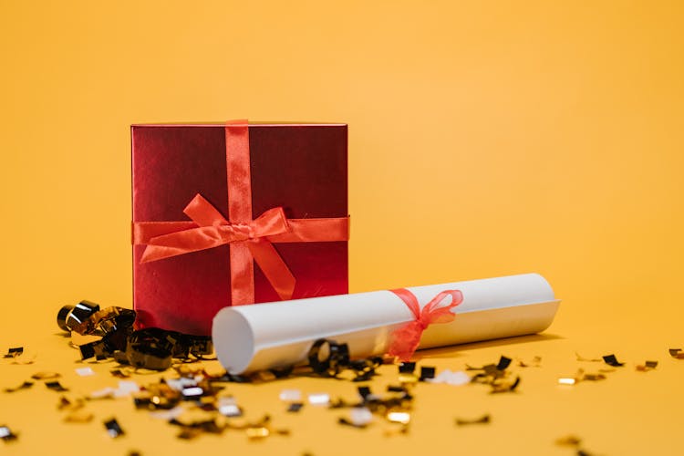 A Rolled Paper And A Box Of Gift On Yellow Surface