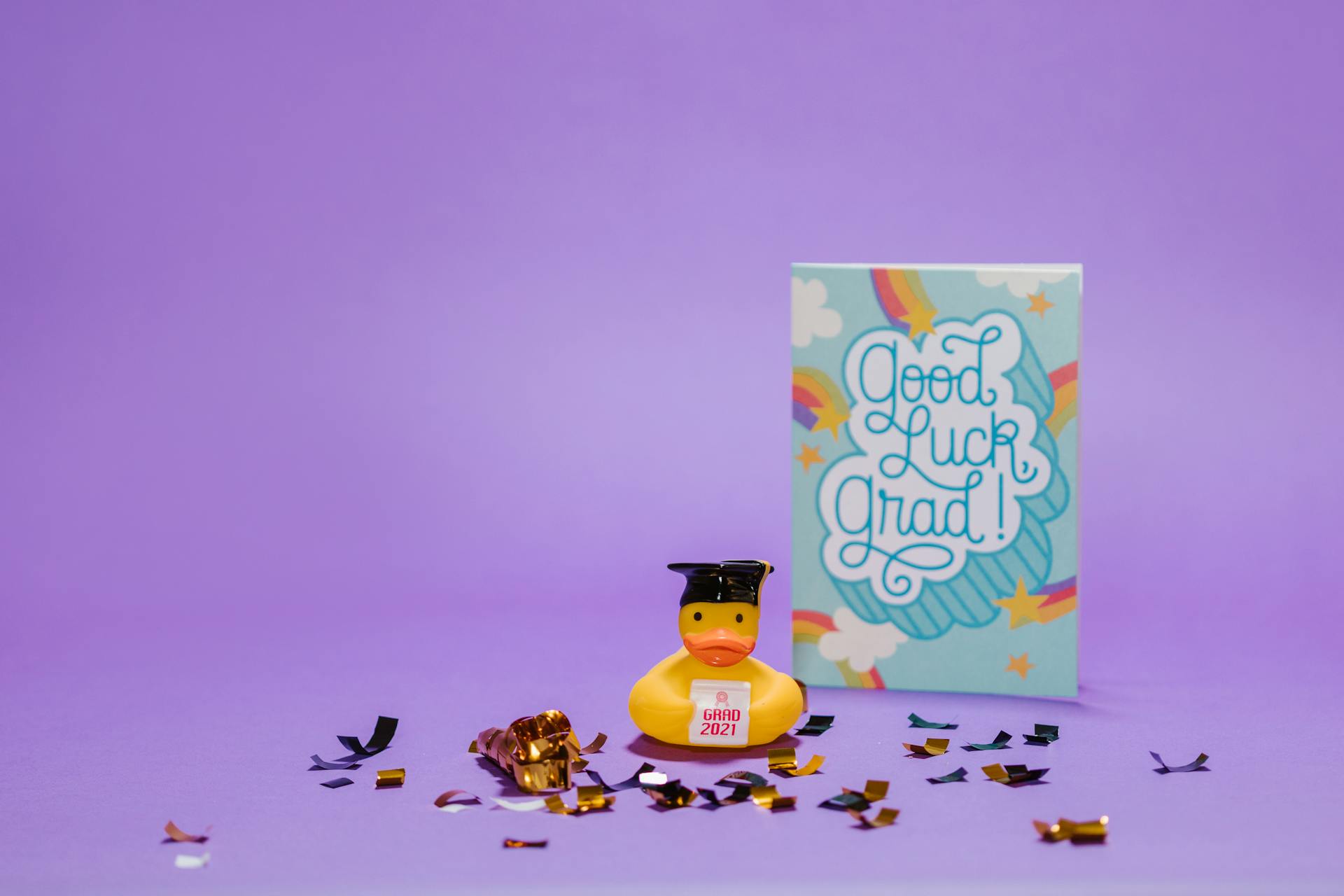 A fun graduation scene with a rubber duck and Good Luck Grad card on purple background.