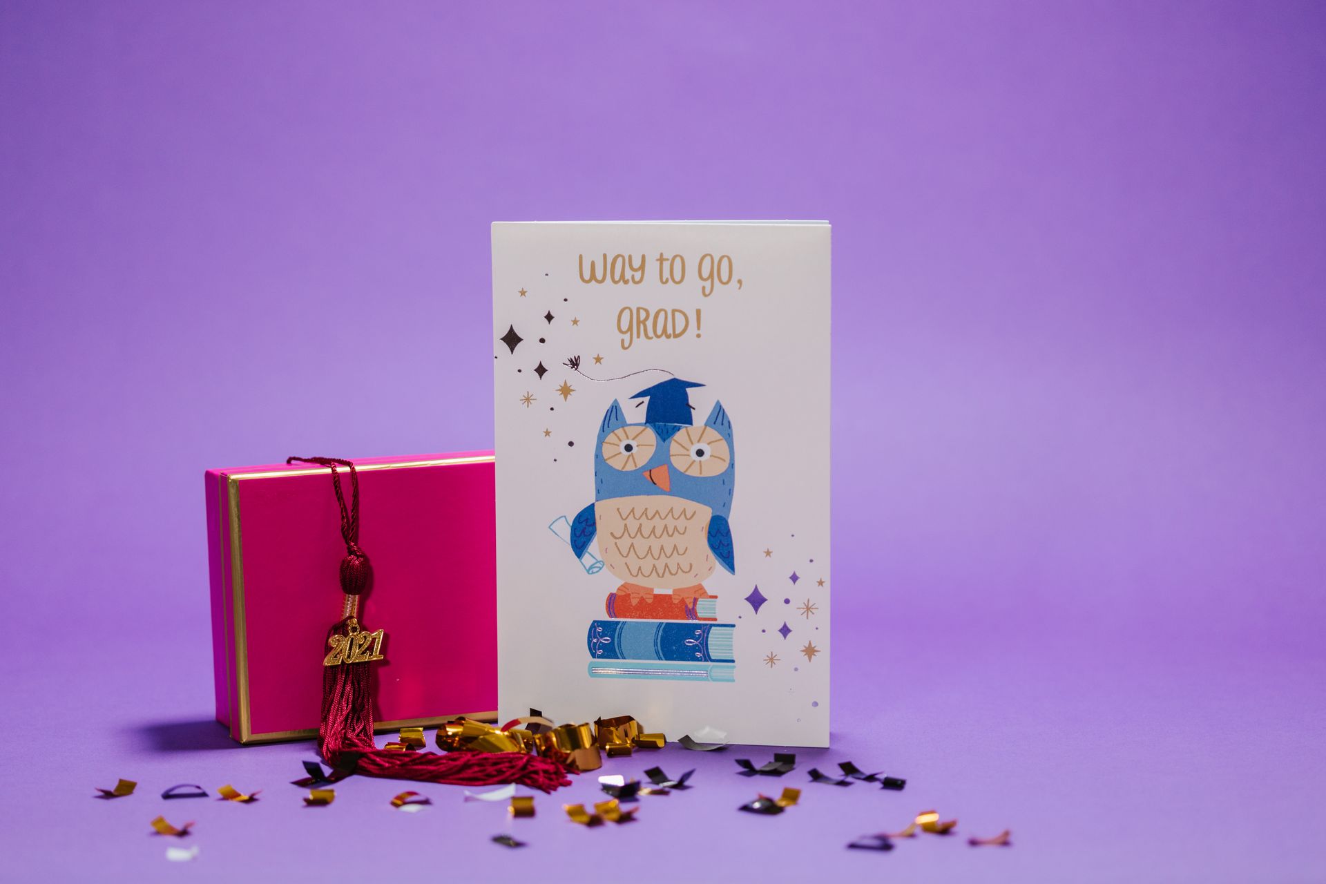 Festive graduation card featuring an owl design, tassel, and colorful confetti on a purple background.