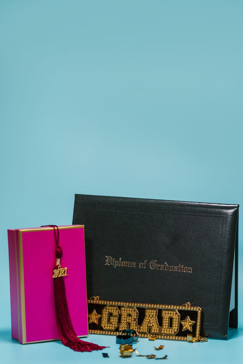 Graduation diploma with gift box, cap tassel, and Grad decor on a blue background.