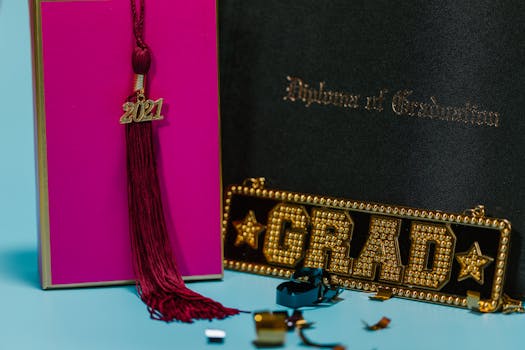A close-up of a graduation tassel dated 2021, a diploma and a glitzy grad sign on a colorful background.