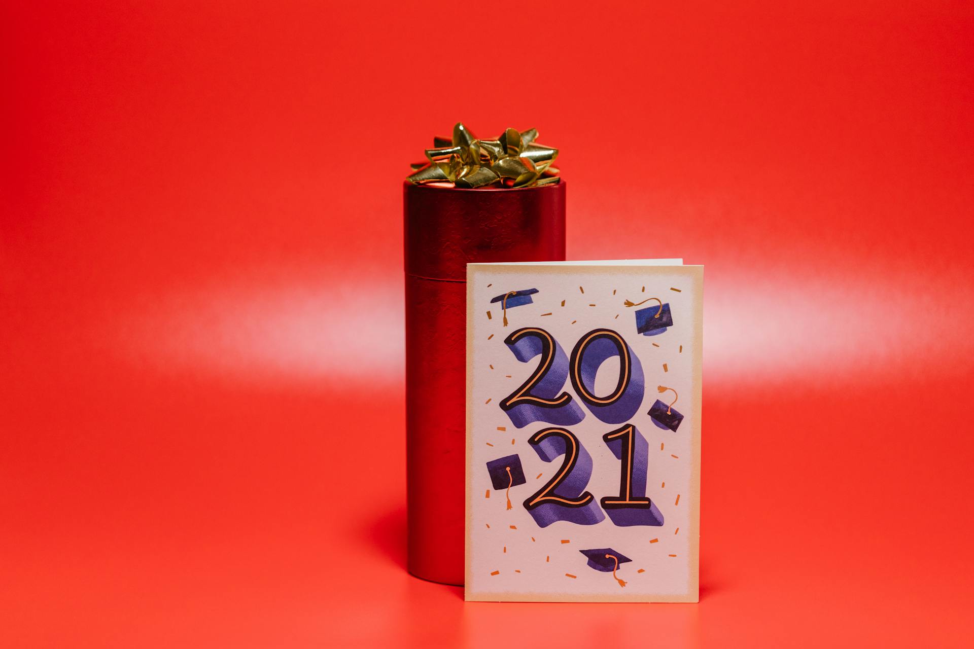 A celebration card displaying '2021' beside a wrapped gift with a gold ribbon on a vibrant red backdrop.