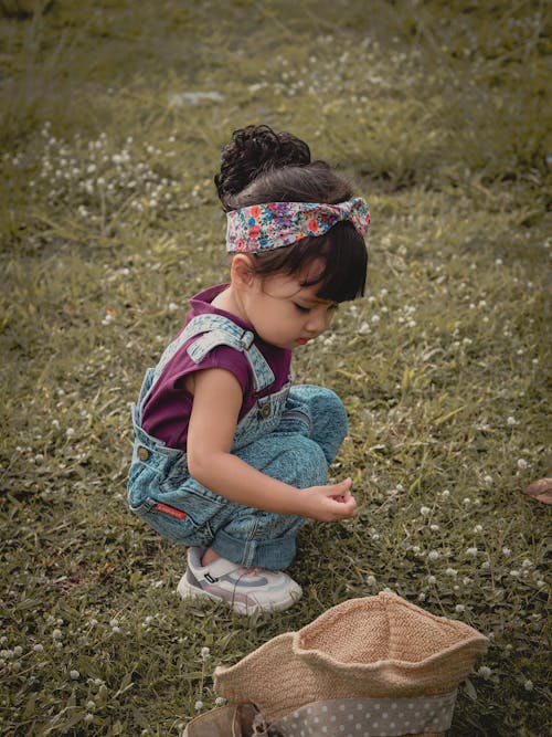 A Girl in Blue Denim Dungaree Sitting on Green Grass