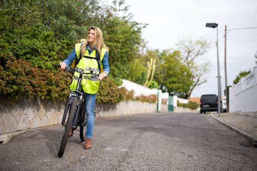 Free A Woman in Yellow Vest and Blue Denim Pants Sitting on Black Bicycle Stock Photo