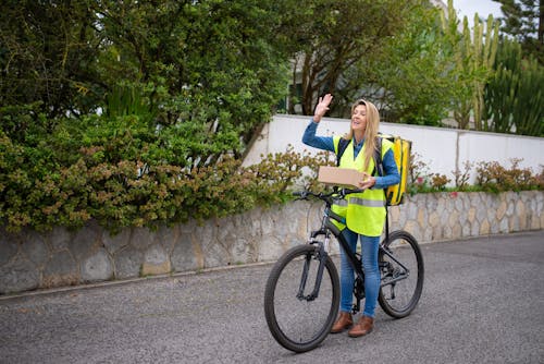 A Delivery Person Waving her Hand while Holding a Package