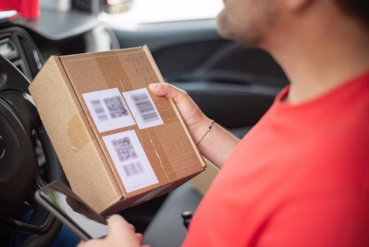Close-up of a person holding a package with QR codes inside a car, emphasizing delivery and technology.