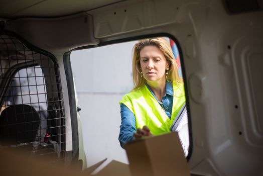 Woman in hi-vis vest organizing boxes inside a delivery van, representing logistics and transportation.