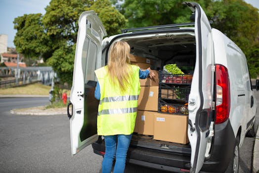 A woman in a reflective vest loads groceries and packages into a delivery van on a sunny day in Portugal.