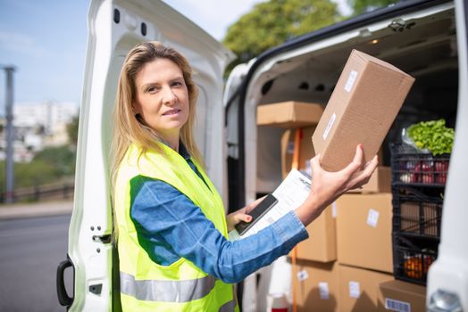 Courier woman in a high-vis vest delivering packages from a van outdoors.