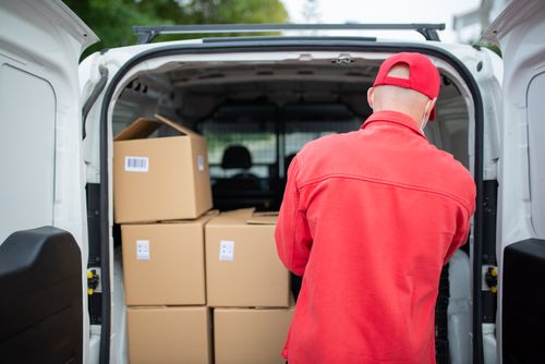 Free Courier in red loading cardboard boxes into a delivery van outdoors in Portugal. Stock Photo