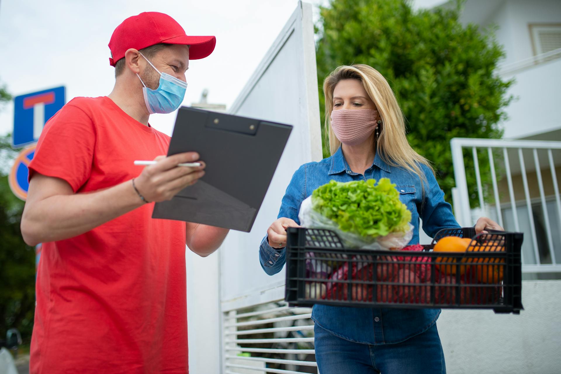 A delivery person in protective gear handing groceries to a customer at home.