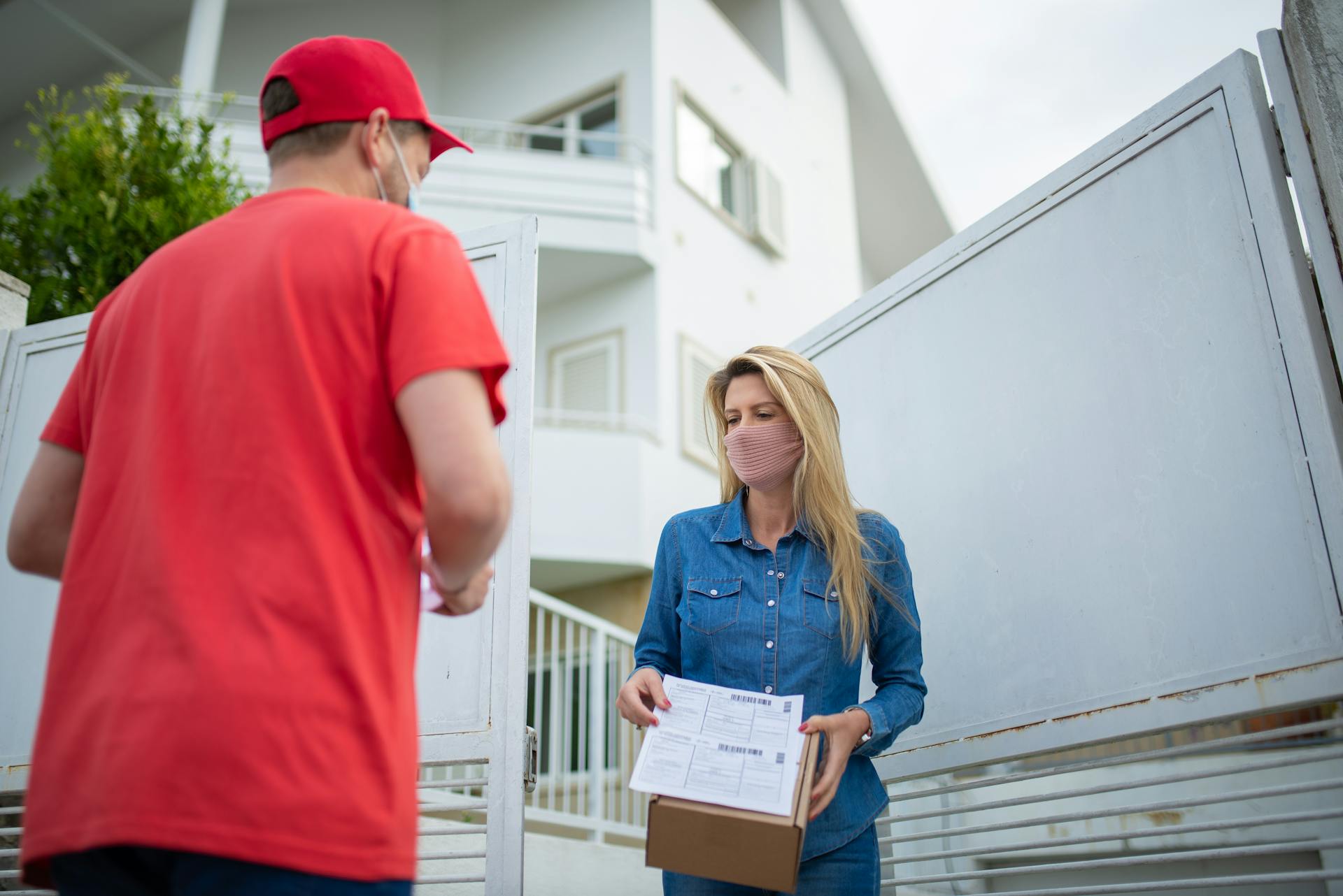 Delivery person handing package to woman wearing mask at home front door.