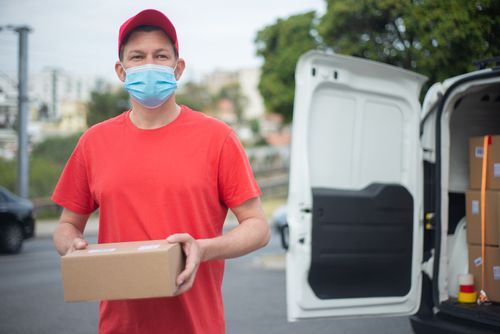 Free Courier in red delivering packages, wearing a mask outdoors in Portugal. Stock Photo