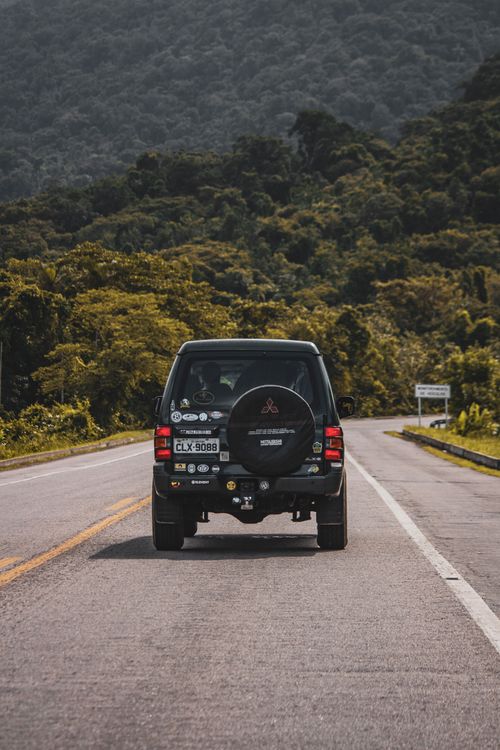Free SUV car driving along asphalt roadway towards hill covered with green woods during road trip Stock Photo