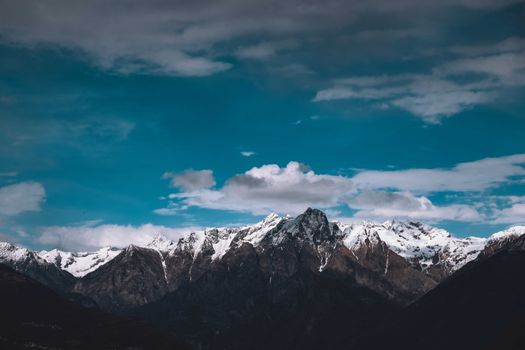 Picturesque view of high mountain peaks covered with snow under blue cloudy heaven