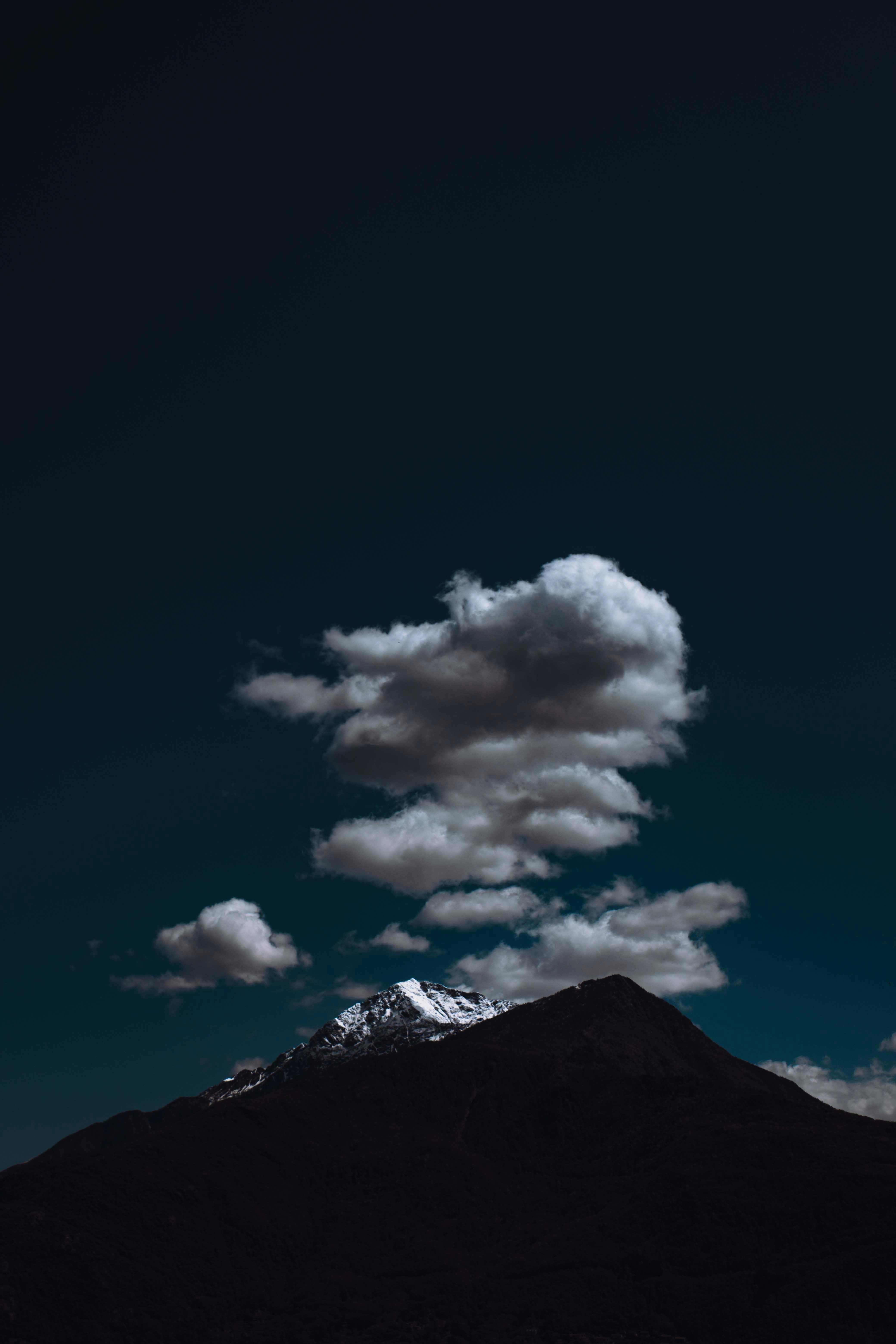 High rocky mountain silhouette covered with snow under dark blue cloudy sky in evening