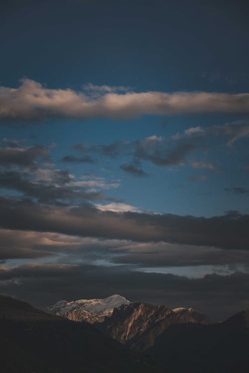 Picturesque view of high mountains with peaks under cloudy dark blue sky in twilight
