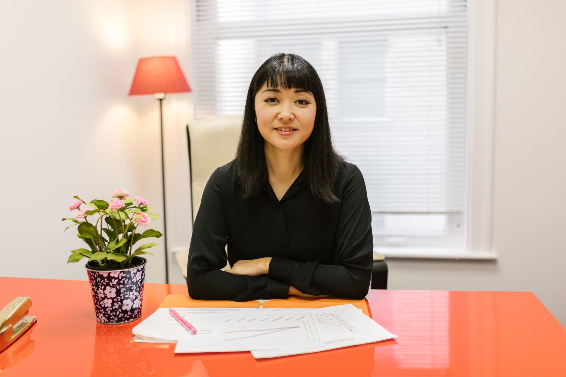 Asian businesswoman smiling at desk in modern office setting, portraying professionalism.