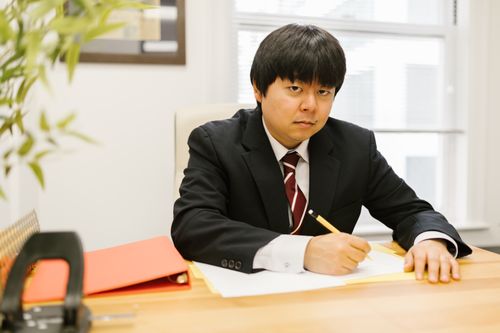 Free Man in a black suit with a pencil working at a desk in an office setting. Stock Photo