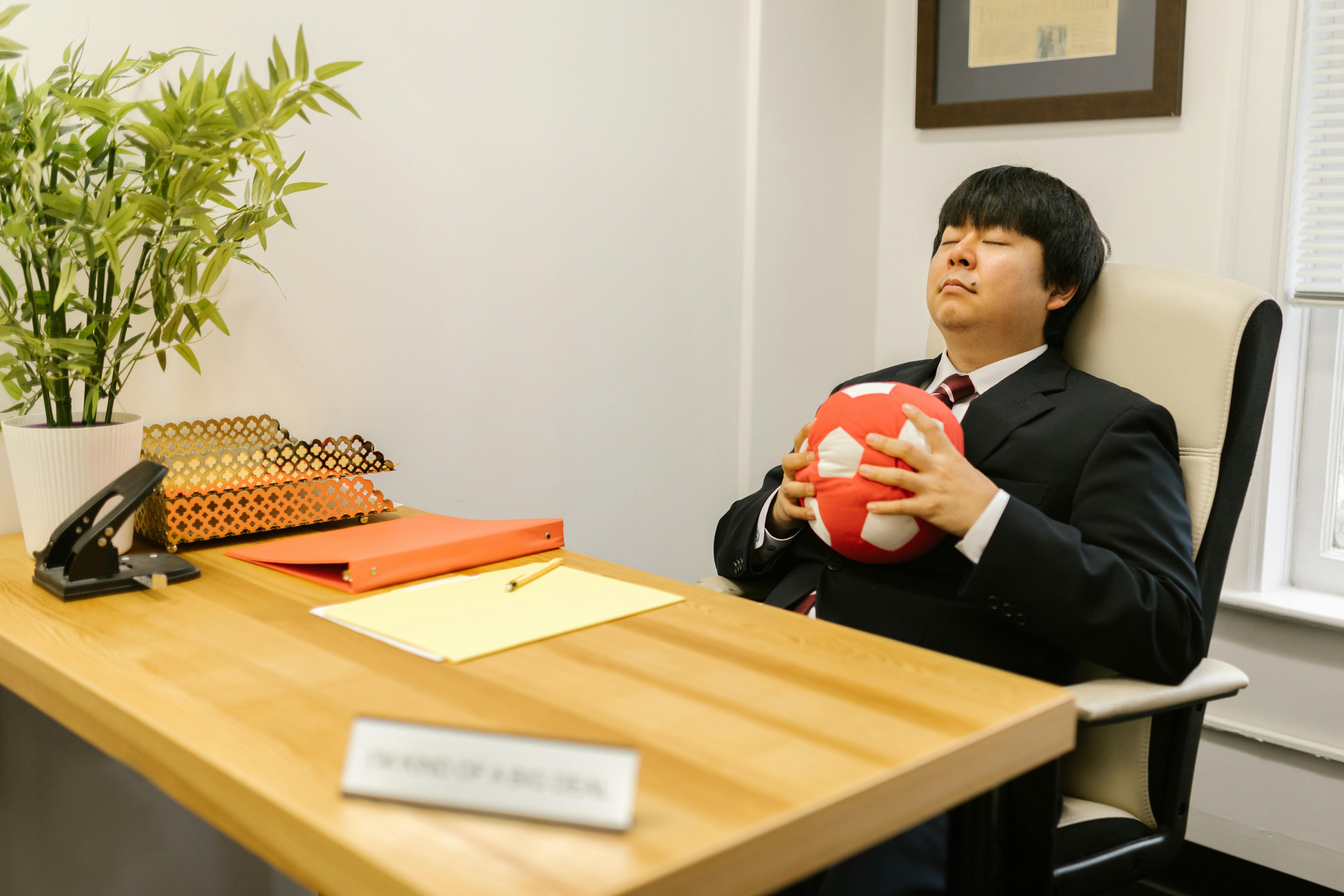 A businessman in a suit relaxes with a stress ball at his work desk for a moment's break.