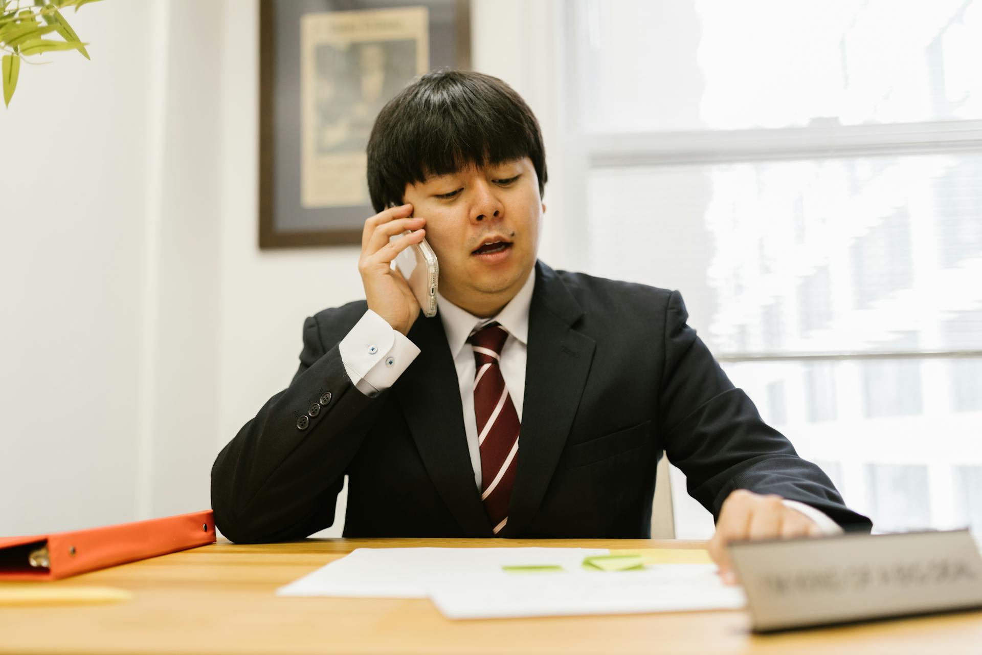 Asian businessman in black suit talking on phone at desk in office