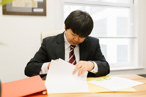 Free Businessperson in a suit examines papers at a desk indoors, focused and diligent. Stock Photo