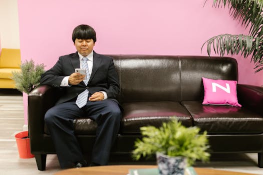 Asian businessman in suit using cellphone on leather sofa in a modern office.