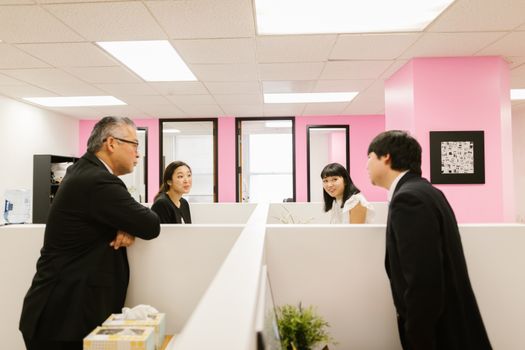 A group of Asian colleagues engaged in a lively discussion in a modern office setting.